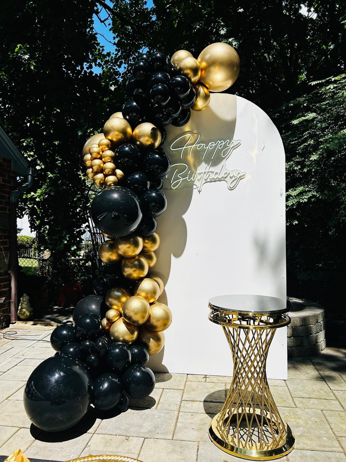 Black and gold balloon garland backdrop with a Happy Birthday neon sign for an adult birthday