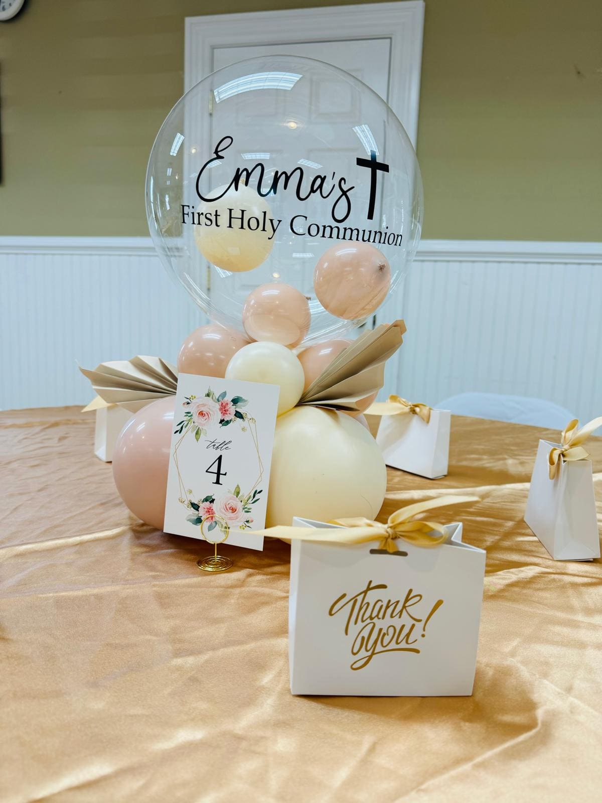 Personalized bubble balloon centerpiece reading Emma's First Holy Communion with a table number